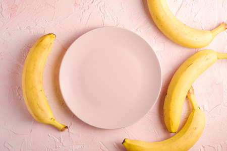 Banana fruits with empty pink plate on pink textured background, top view copy spaceの写真素材