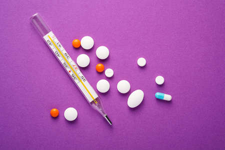Pills, tablets and analog thermometer on violet purple background, healthcare medical concept,...