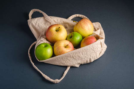 Fresh sweet apples in reusable textile grocery bag on dark grey background, angle viewの写真素材
