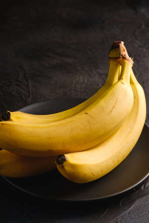 Banana fruits in black plate on dark textured background, angle view macroの写真素材