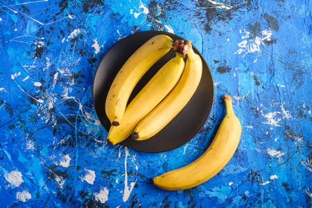 Banana fruits in black plate on blue textured background, top view copy spaceの写真素材