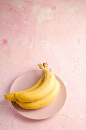 Banana fruits in pink plate on pink textured background, angle view copy spaceの写真素材