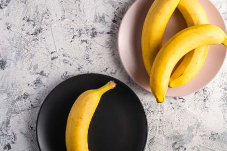 Banana fruits in pink and black plates on white textured background, top view copy spaceの写真素材