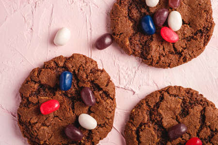 Homemade oat chocolate cookies with cereal with juicy jelly beans on textured pink background, top view macroの写真素材