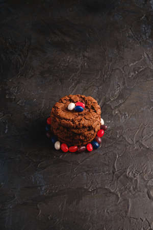 Homemade oat chocolate cookies stack with cereal with juicy jelly beans on textured dark black background, angle viewの写真素材