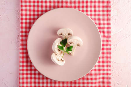 Champignon mushrooms healthy food in pink plate with parsley greenery on red tablecloth on pink textured background, top viewの写真素材