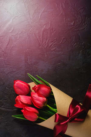 Bouquet with bow-knot ribbon of red tulip flowers on textured black background, top view copy spaceの写真素材