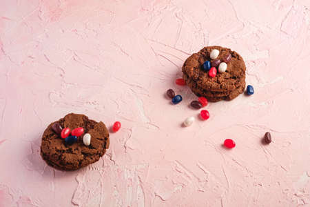 Homemade oat chocolate cookies stack with cereal with juicy jelly beans on textured pink background, angle view copy spaceの写真素材