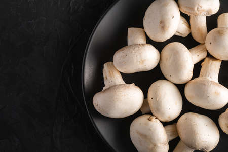 Champignon mushrooms healthy food on black plate on dark black textured background, top viewの写真素材