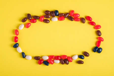 Round frame of juicy sweet fruit colorful jelly beans on bright yellow background, top view copy spaceの写真素材
