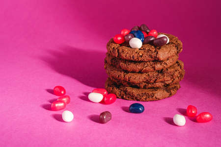 Homemade oat chocolate cookies stack with cereal with juicy jelly beans on minimal pink purple background, angle viewの写真素材