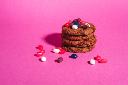 Homemade oat chocolate cookies stack with cereal with juicy jelly beans on minimal pink purple background, angle view copy spaceの写真素材