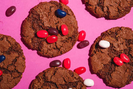 Homemade oat chocolate cookies with cereal with juicy jelly beans on minimal pink purple background, top view macroの写真素材