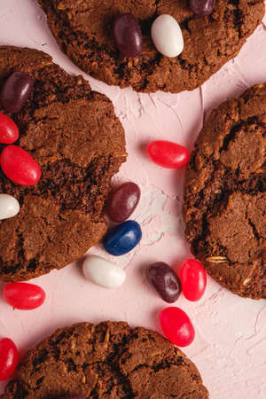 Homemade oat chocolate cookies with cereal with juicy jelly beans on textured pink background, top...