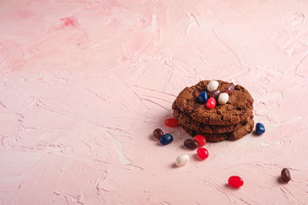 Homemade oat chocolate cookies stack with cereal with juicy jelly beans on textured pink background, angle view copy spaceの写真素材