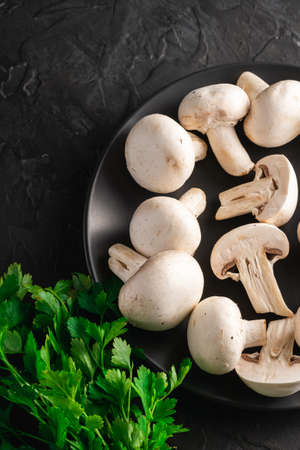 Champignon mushrooms healthy food on black plate with parsley greenery on dark black textured background, angle viewの写真素材