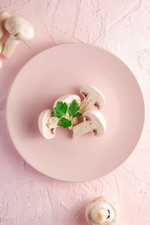 Champignon mushrooms healthy food on pink plate with parsley greenery on pink textured background, top viewの写真素材