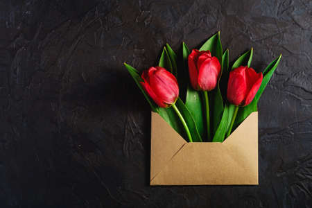 Bunch of red tulip flowers in paper envelope on textured dark black background, top view copy spaceの写真素材