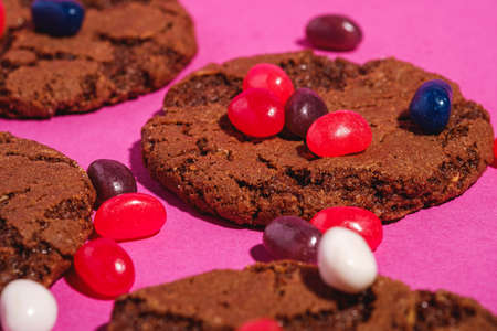 Homemade oat chocolate cookies with cereal with juicy jelly beans on minimal pink purple background, angle view macroの写真素材