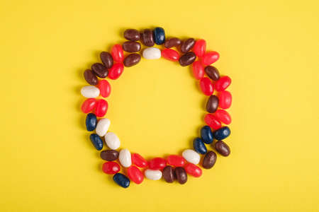 Round frame of juicy sweet fruit colorful jelly beans on bright yellow background, top view copy spaceの写真素材