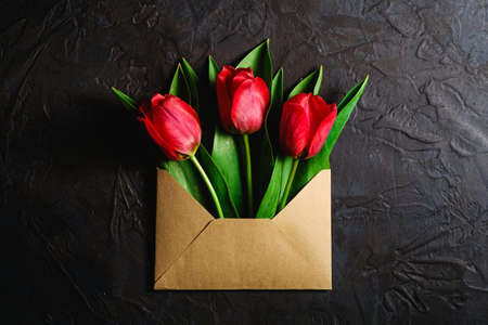 Bunch of red tulip flowers in paper envelope on textured dark black background, top view copy spaceの写真素材