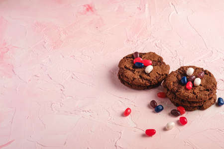 Homemade oat chocolate cookies stack with cereal with juicy jelly beans on textured pink background, angle view copy spaceの写真素材
