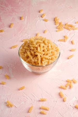 Raw wheat golden spiral pasta in glass bowl on textured pink background, angle viewの写真素材
