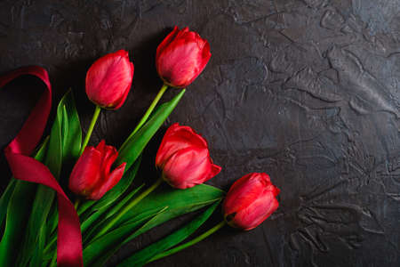 Red bunch of tulip flowers with red ribbon on textured black background, top view copy spaceの写真素材