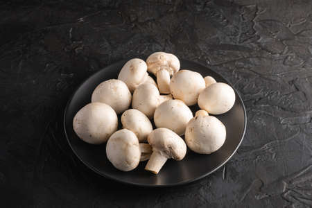 Champignon mushrooms healthy food on black plate on dark black textured background, angle view copy spaceの写真素材