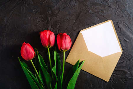 Red bunch of tulip flowers with envelope card on textured black background, top view copy spaceの写真素材