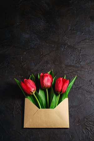 Bunch of red tulip flowers in paper envelope on textured dark black background, top view copy spaceの写真素材