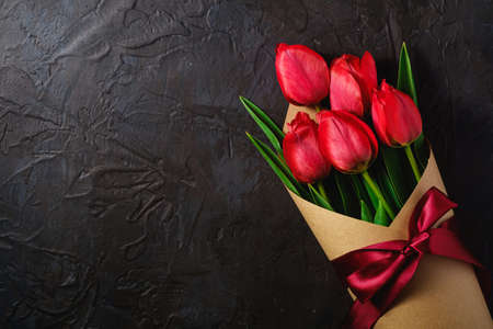 Bouquet with bow-knot ribbon of red tulip flowers on textured black background, top view copy spaceの写真素材