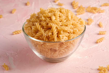Raw wheat golden spiral pasta in glass bowl on textured pink background, angle viewの写真素材