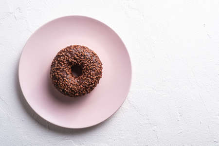 Chocolate donut with sprinkles on pink plate, sweet glazed dessert food on white concrete textured background, top view copy spaceの写真素材