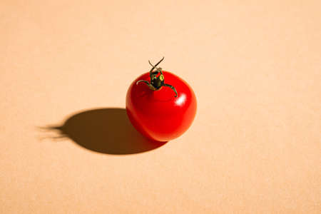 Single cherry tomato vegetable, fresh ripe food on minimal cream colored background, angle viewの写真素材