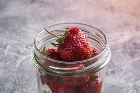 Fresh ripe strawberry fruits in glass jar, summer vitamin berries on grey stone background, angle view macroの写真素材