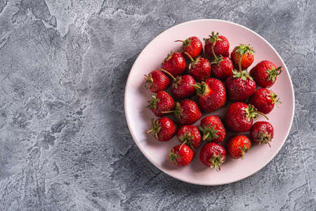 Fresh ripe strawberry fruits in pink plate, summer vitamin berries on grey stone background, top view copy spaceの写真素材