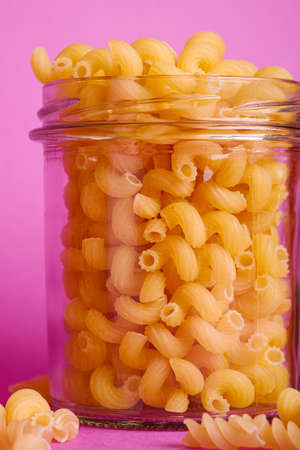 One glass jar with cavatappi uncooked golden wheat curly pasta on minimal pink background, angle view macroの写真素材