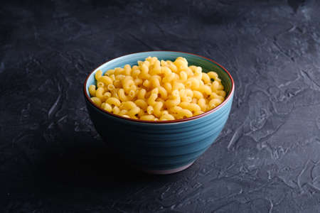 Blue bowl with cavatappi uncooked golden wheat curly pasta on textured dark black background, angle viewの写真素材