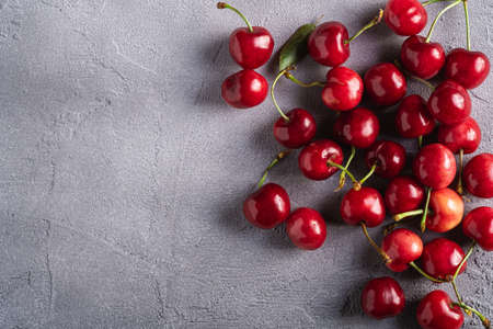 Fresh ripe cherry fruits with green leaves, summer vitamin berries on grey stone background, top view copy spaceの写真素材