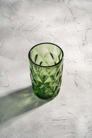 Green glass geometric cup with colorful shadow light rays on stone concrete background, angle viewの写真素材
