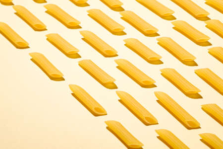 Italian pasta, raw penne tube macaroni pattern on yellow cream background, angle view, abstract food