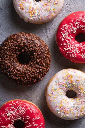 Chocolate, pink and vanilla donuts with sprinkles, sweet glazed dessert food on concrete textured background, top view macroの写真素材