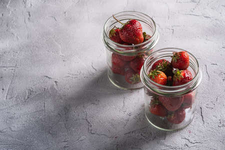 Fresh ripe strawberry fruits in two glass jars, summer vitamin berries on grey stone background, angle view copy spaceの写真素材