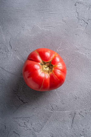 One pink heirloom tomato vegetable, fresh red ripe tomatoes, vegan food, stone concrete background, top viewの写真素材