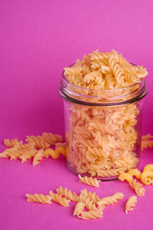 One glass jar with fusilli uncooked golden wheat pasta on minimal pink background, angle view macroの写真素材