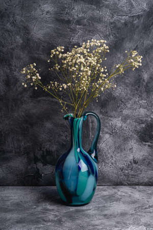 Blue jug vase with bulk gypsophila dried white flowers on dark textured stone background, angle viewの写真素材