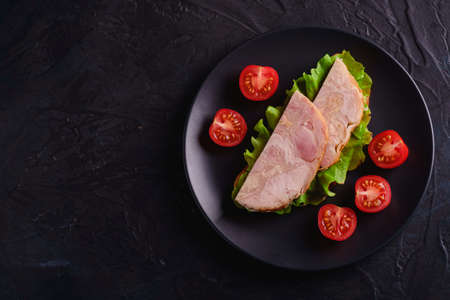 Sandwich with turkey ham meat, green salad and fresh cherry tomatoes slices on black plate, dark textured background, top view copy spaceの写真素材