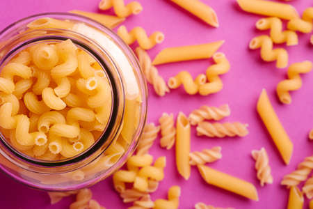 One glass jar with variety of uncooked golden wheat pasta on minimal pink background, top view macroの写真素材