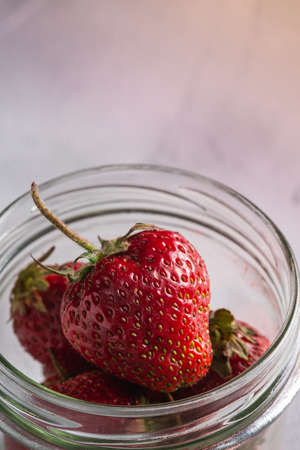 Fresh ripe strawberry fruits in glass jar, summer vitamin berries on grey stone background, angle view macroの写真素材